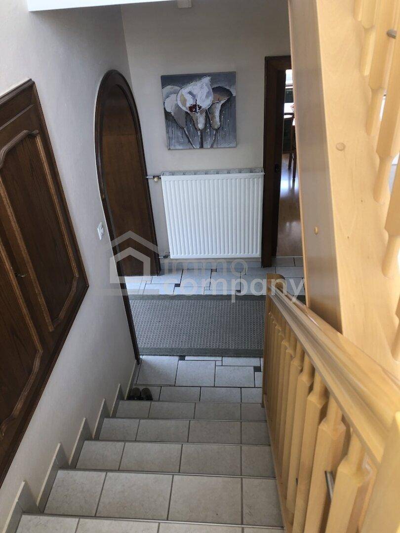 Eingangsbereich mit gefliester Treppe und Holzgeländer, ein Heizkörper ist an der Wand sichtbar.