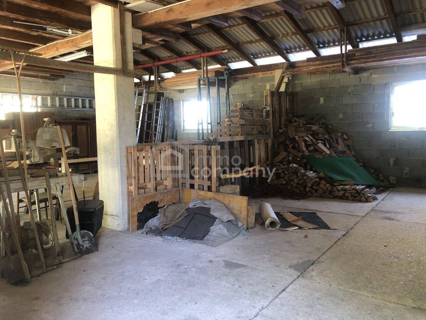 Großer, rustikaler Raum mit Holzbalken und Betonboden, genutzt als Lager oder Werkstatt.