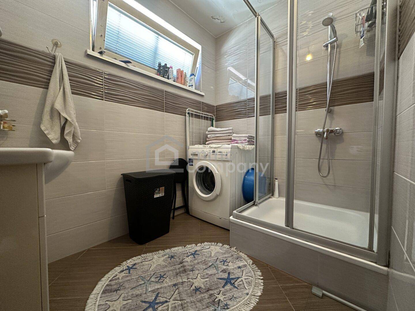 Funktionales Badezimmer mit Duschkabine, Waschmaschine und Fenster.