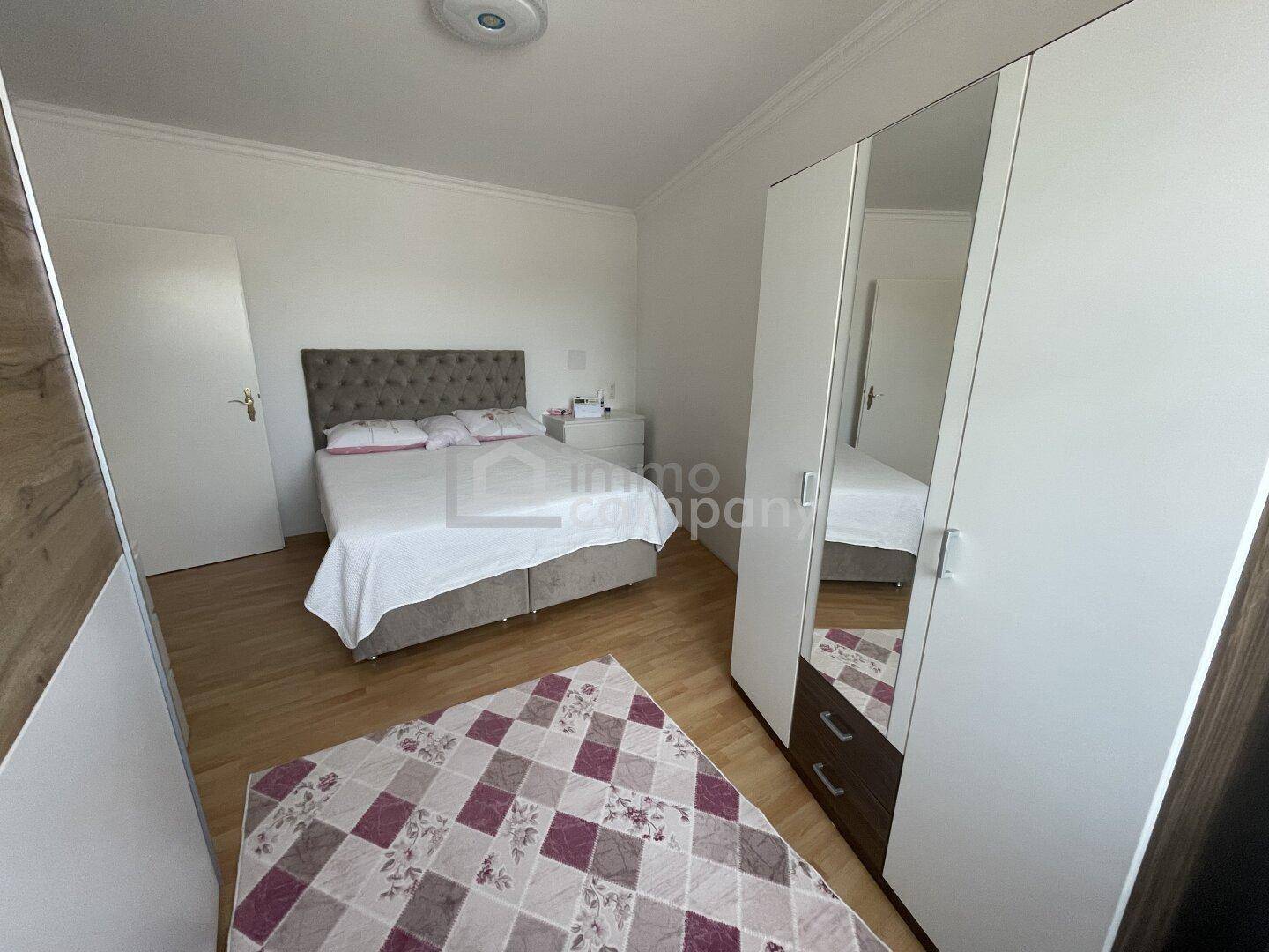 Helles Schlafzimmer mit Doppelbett, Spiegelschrank und Holzfußboden.