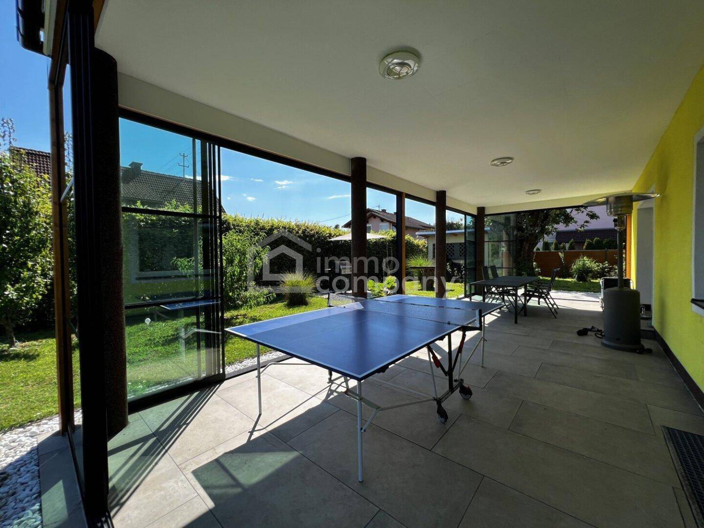 Verglaste Terrasse mit Tischtennisplatte und Blick auf den grünen Garten, ideal für Freizeitaktivitäten.