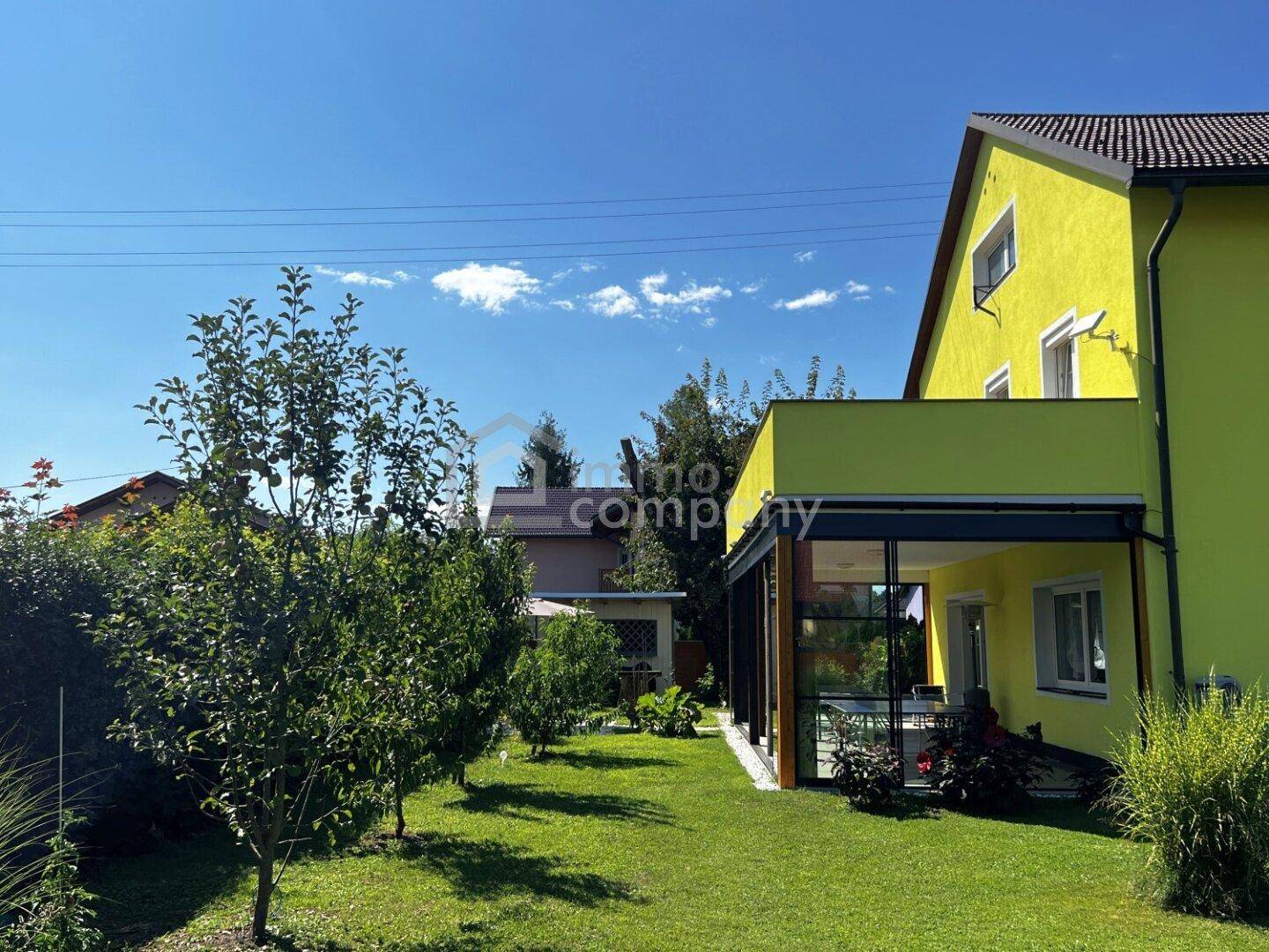 Seitenansicht des gelben Hauses mit großem Garten und üppiger Vegetation unter strahlendem Himmel.