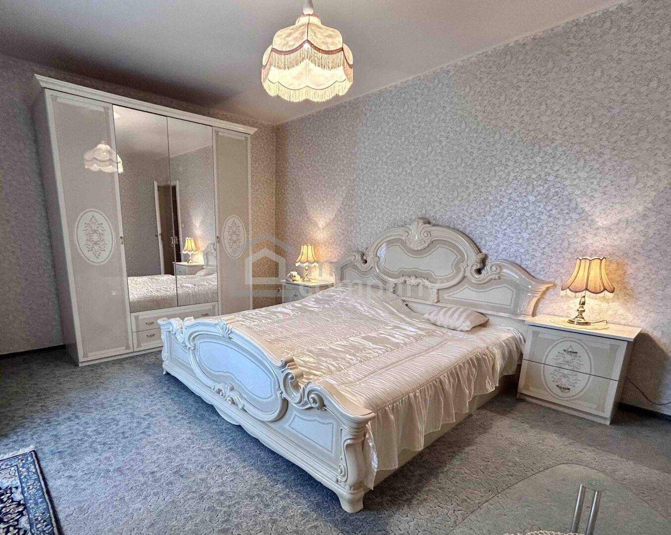 Geräumiges Schlafzimmer mit opulentem weißen Bett, passenden Möbeln und gemusterter Tapete.