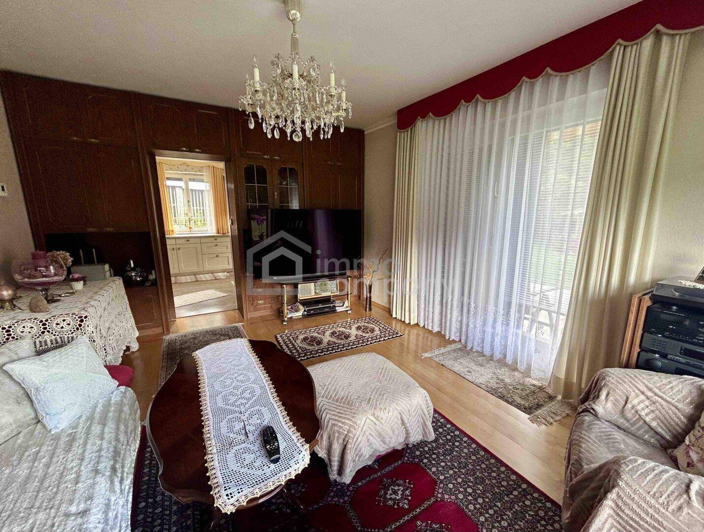 Klassisches Wohnzimmer mit Holzwandmöbeln, Kronleuchter und Blick in die angrenzende Küche.