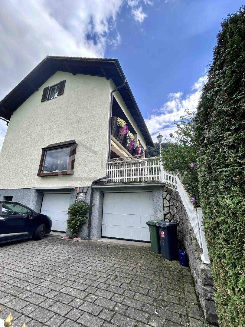 Seitenansicht des Hauses mit zwei Garagen, gepflasterter Auffahrt und einem blumengeschmückten Balkon.