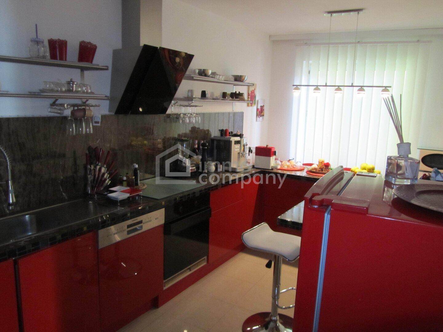 Moderne Küche mit roten Hochglanzfronten, schwarzer Arbeitsplatte und integrierten Geräten sowie Frühstücksbar.