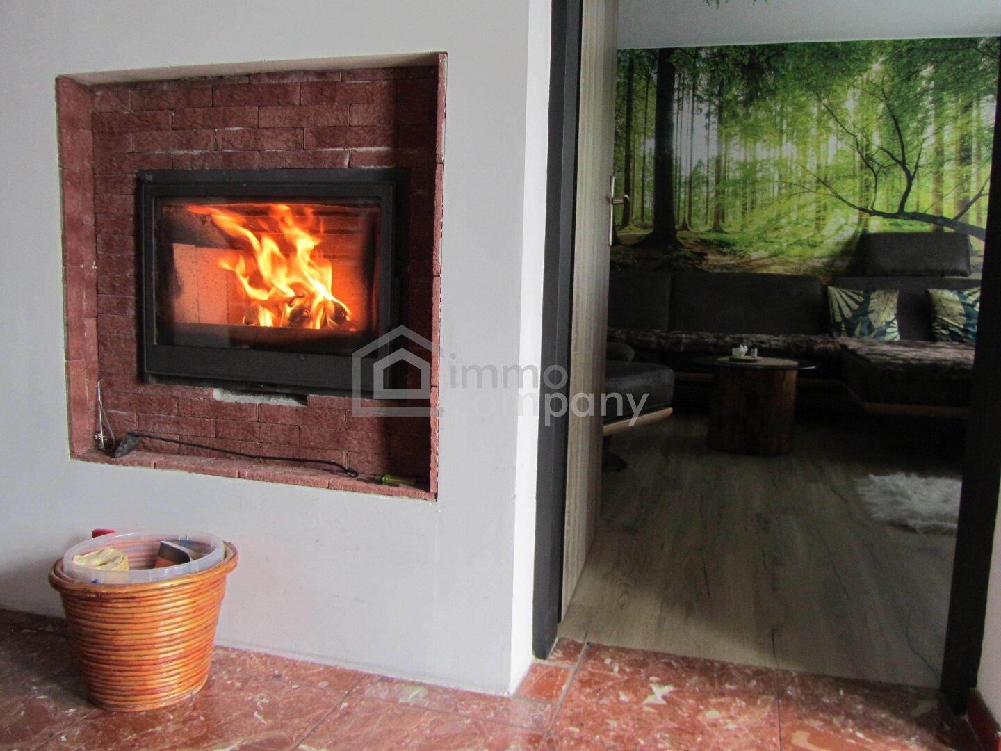 Eingebauter Kamin mit Ziegelverkleidung und brennendem Feuer, der zum Wohnbereich führt.