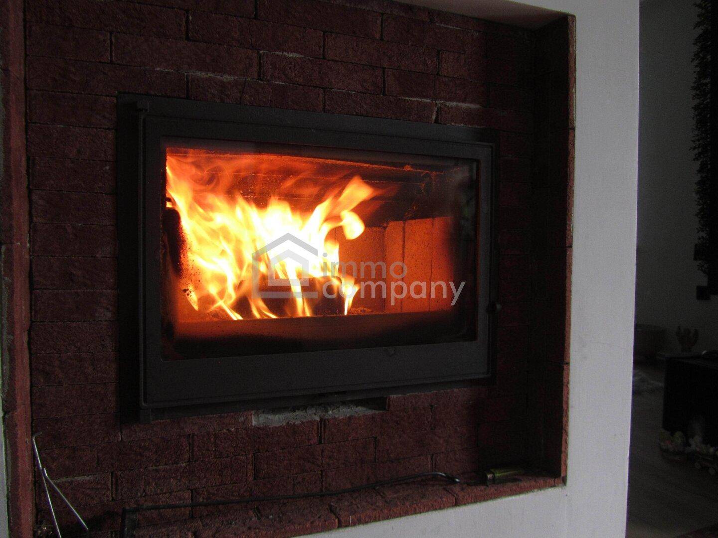 Nahaufnahme eines Kamins mit loderndem Feuer und rustikaler Ziegelumrandung, die Wärme spendet.