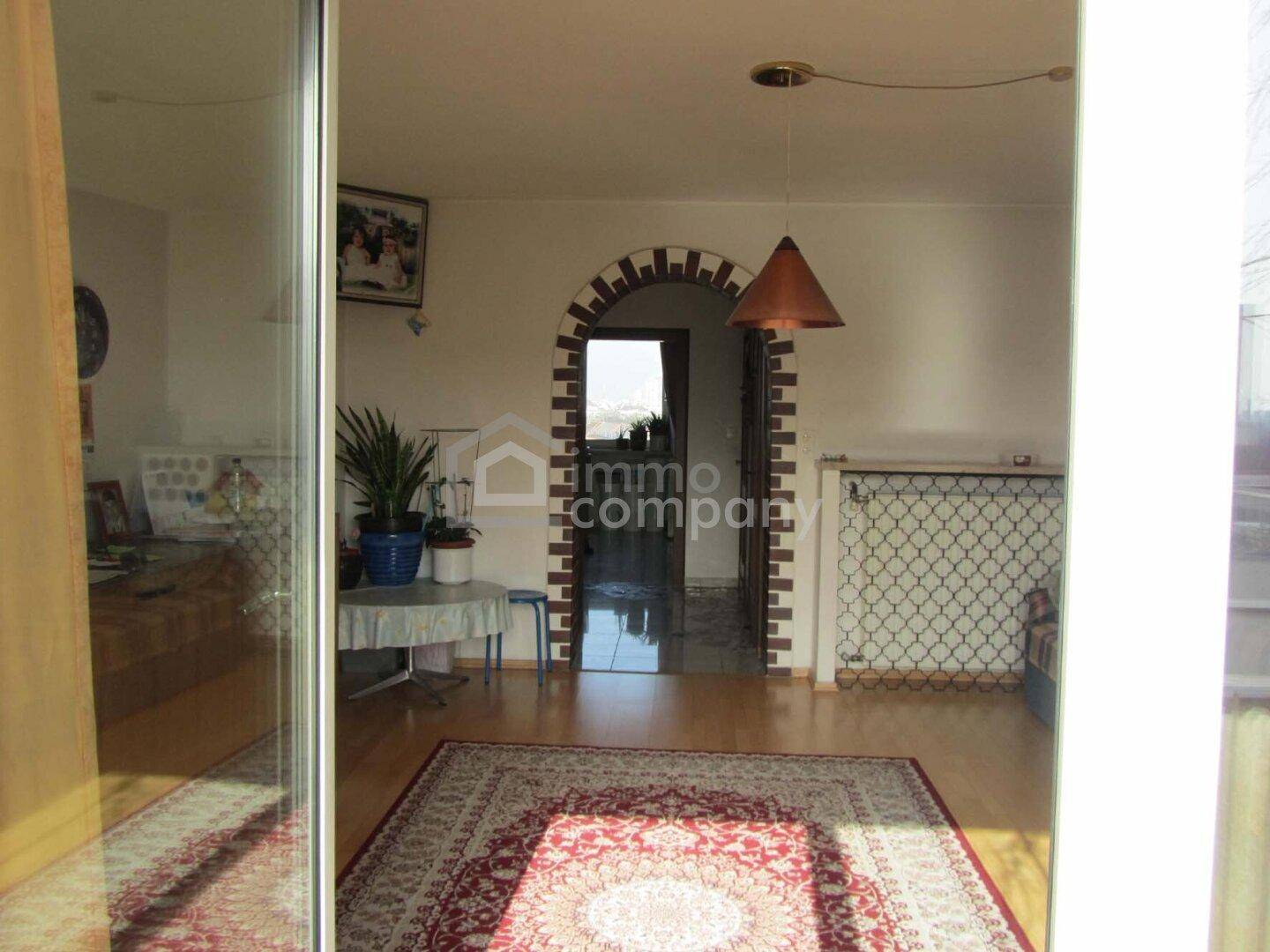 Blick vom Balkon in einen hellen Wohnbereich mit Teppich, Pflanzen und einem dekorativen Bogen.