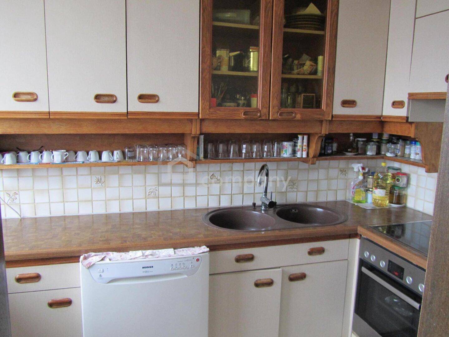 Funktionale Küche mit hellen Schränken, Holzdetails, Doppelspüle und integrierten Geräten.