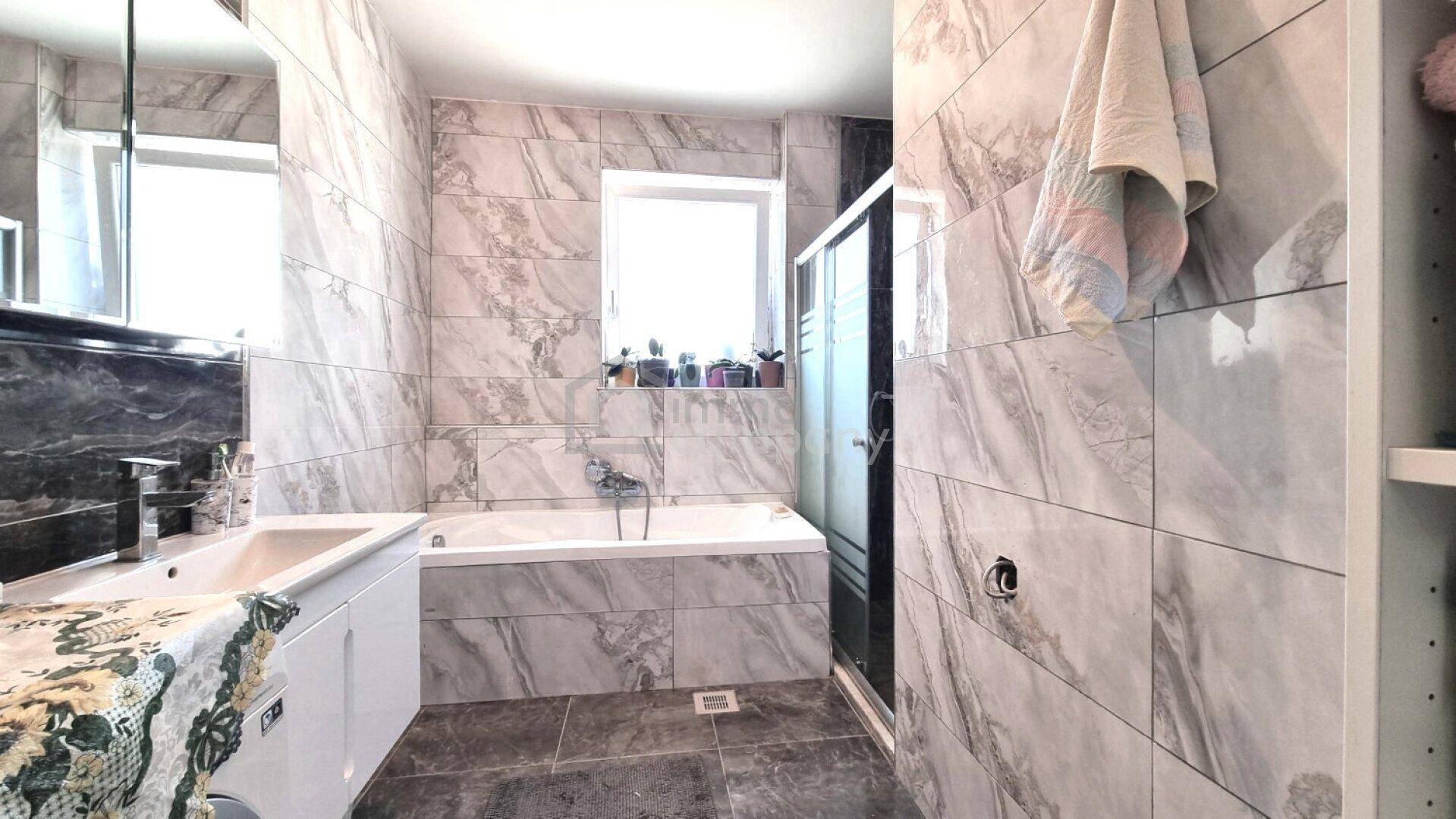 Modernes Badezimmer mit Marmorfliesen, Badewanne, begehbarer Dusche und Fenster.
