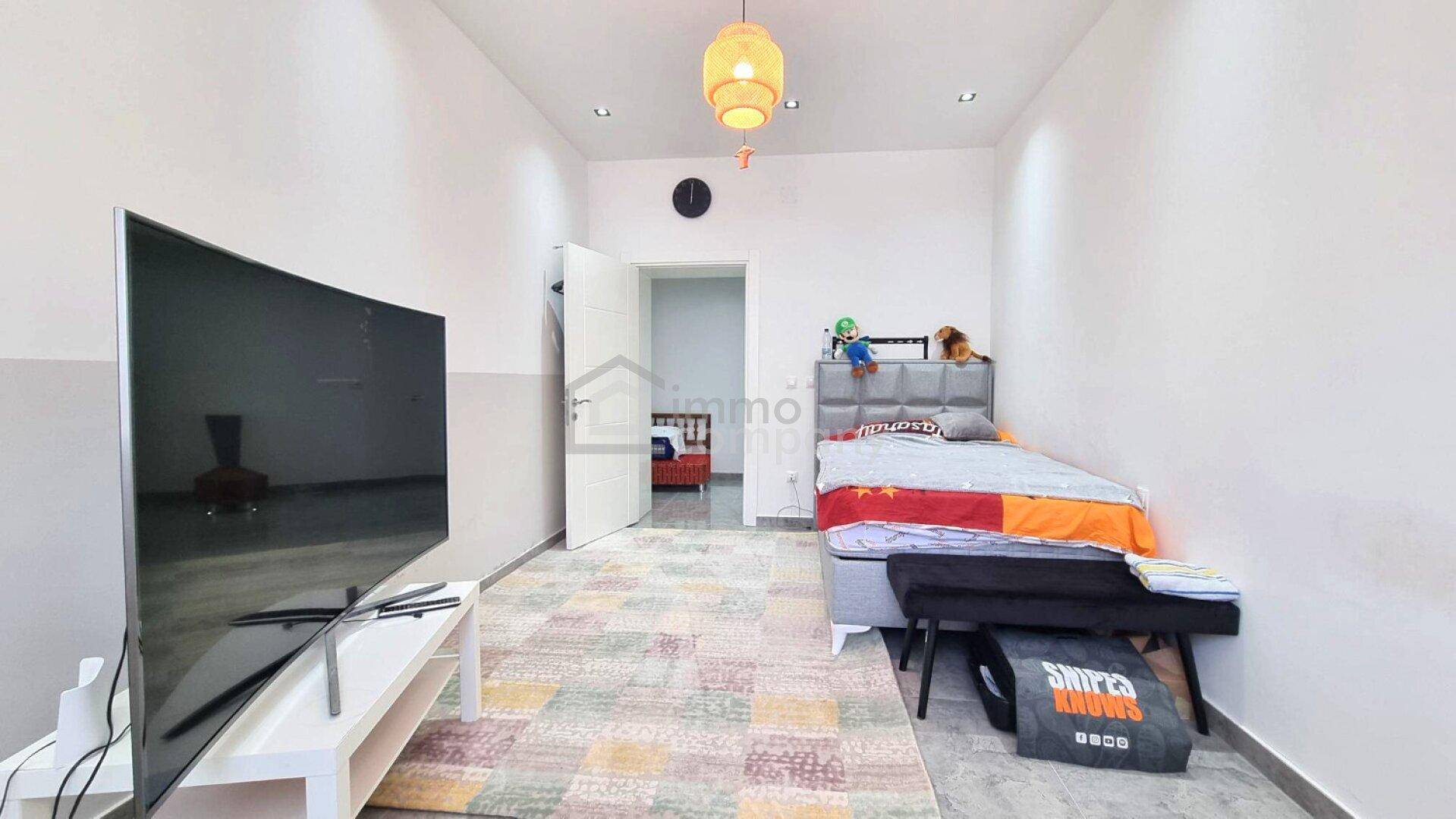 Helles Kinderzimmer mit Einzelbett, Fernseher und Zugang zu einem weiteren Raum.