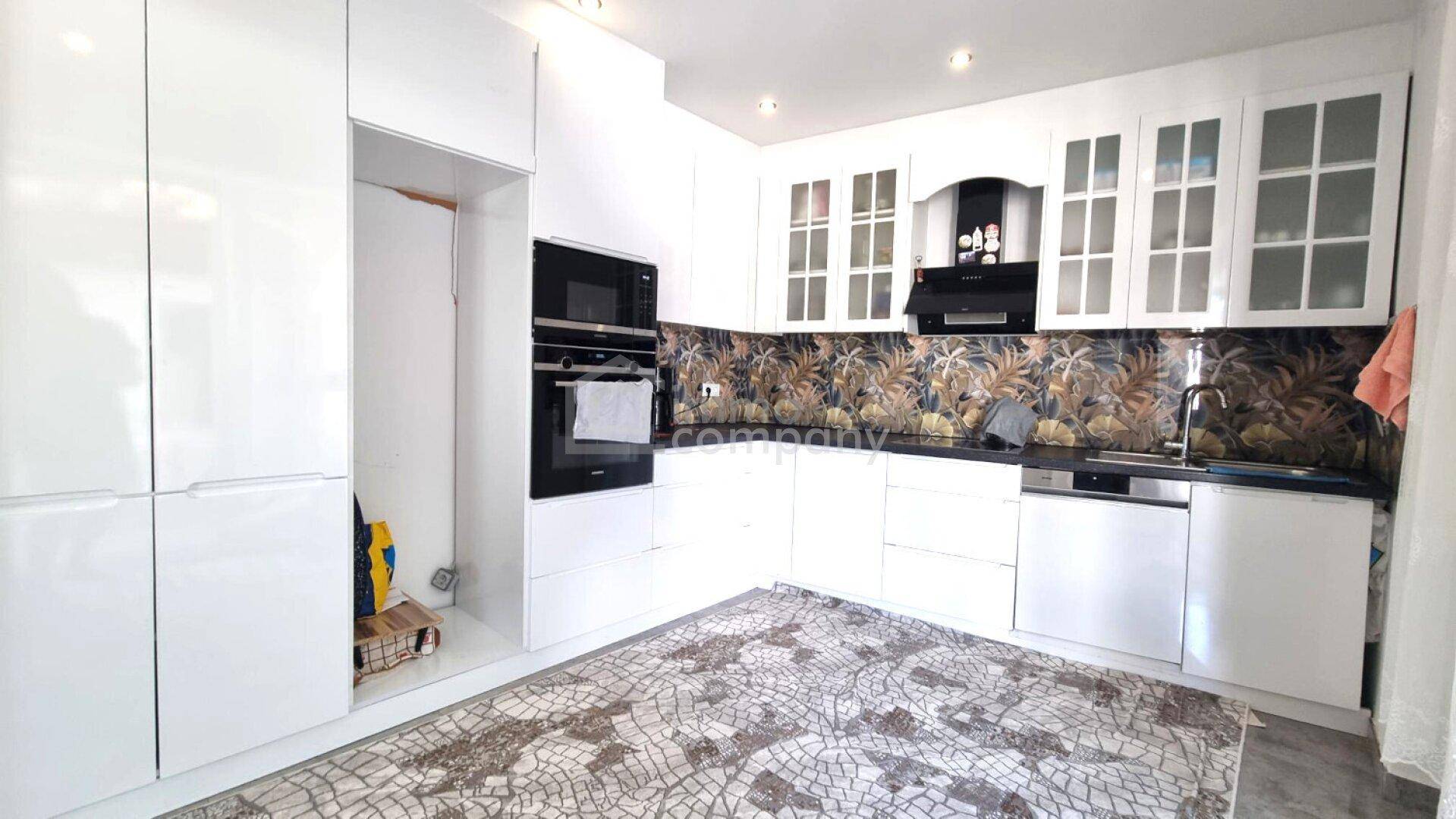 Moderne Küche mit weißen Hochglanzschränken, integrierten Geräten und dekorativem Fliesenspiegel.