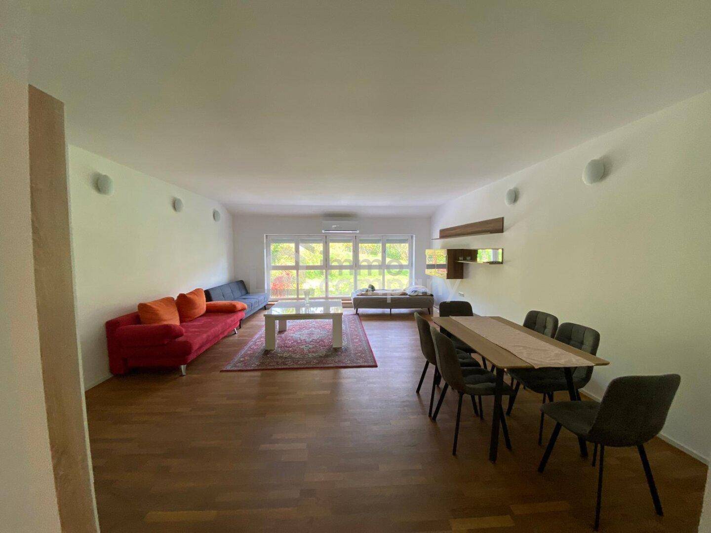 Geräumiger Wohn-Essbereich mit Holzboden, farbigen Sofas und viel Tageslicht.