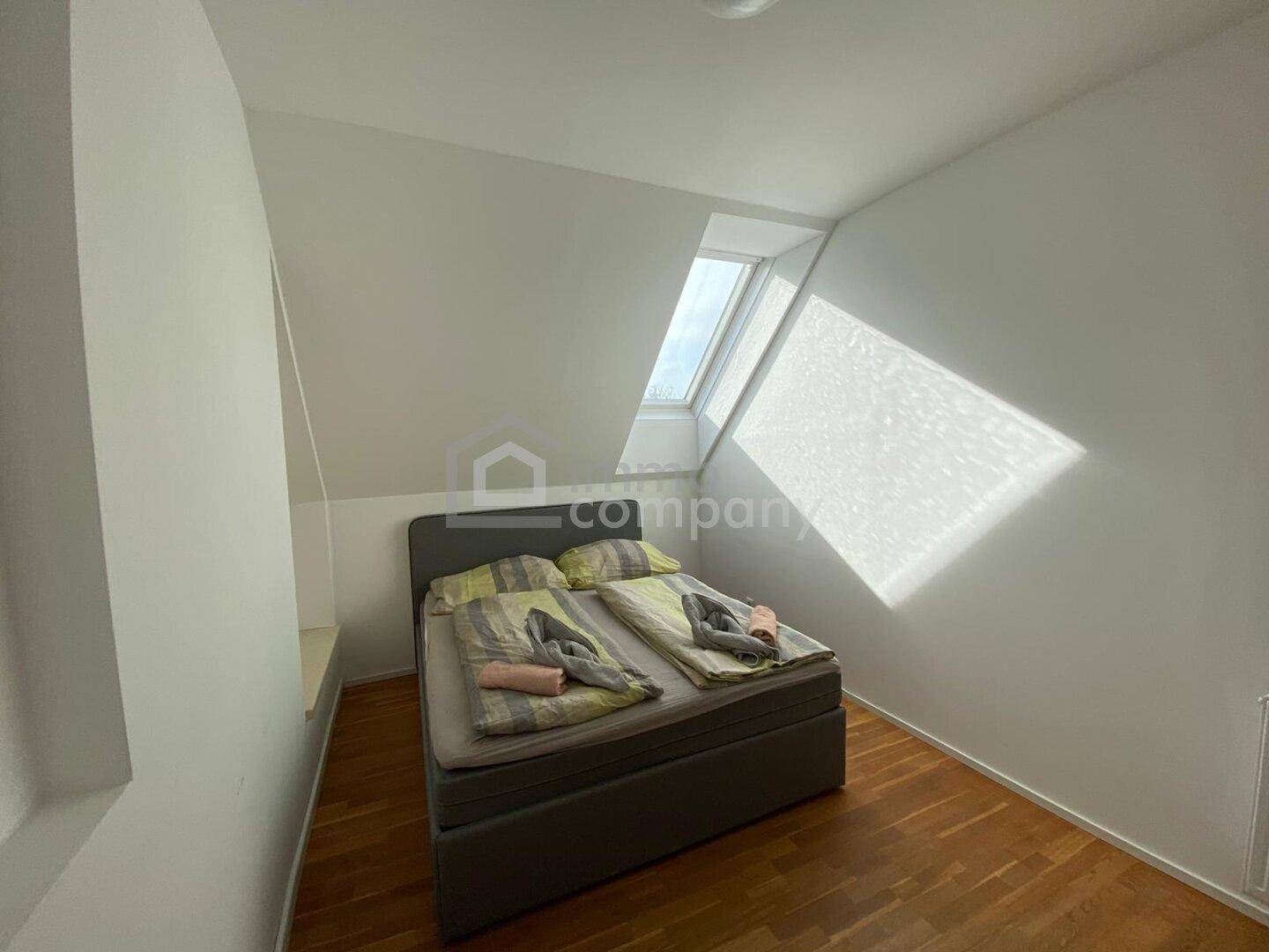 Helles Schlafzimmer im Dachgeschoss mit Dachfenster, Holzboden und schrägen Wänden.