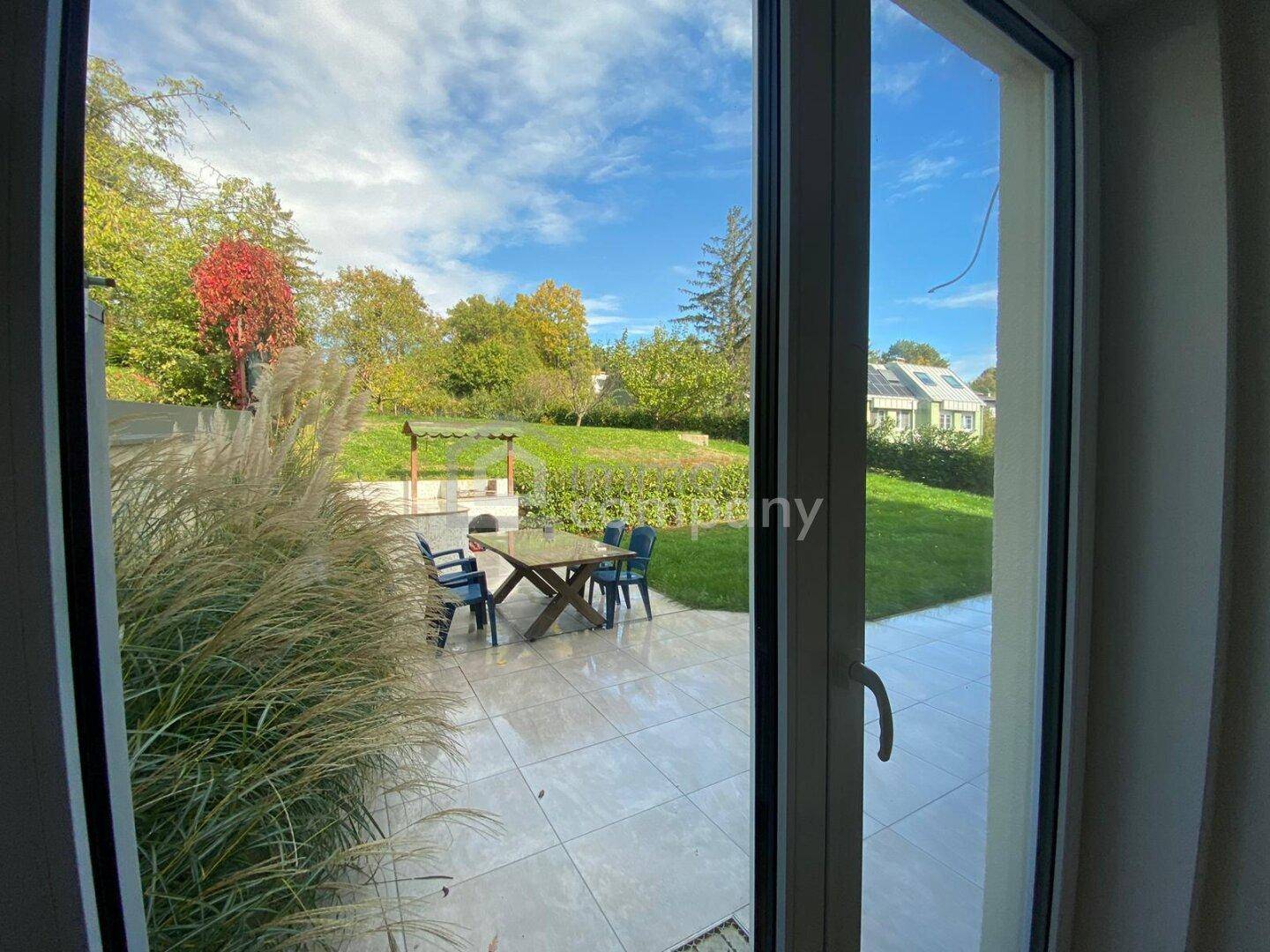 Blick vom Innenraum durch große Fenster auf die Terrasse und den weitläufigen grünen Garten.
