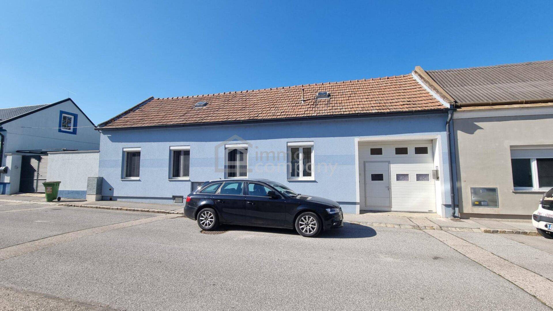 Ansicht des Hauses von der Straße mit blauer Fassade und Garagentor.