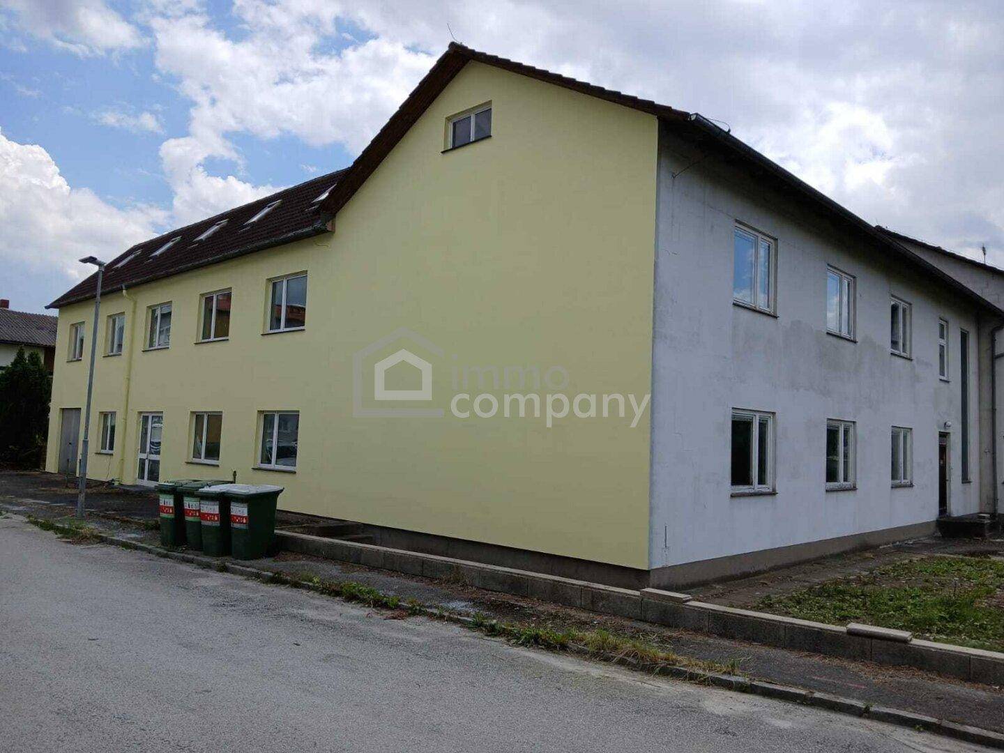 Mehrfamilienhaus mit gelber und grauer Fassade unter bewölktem Himmel.