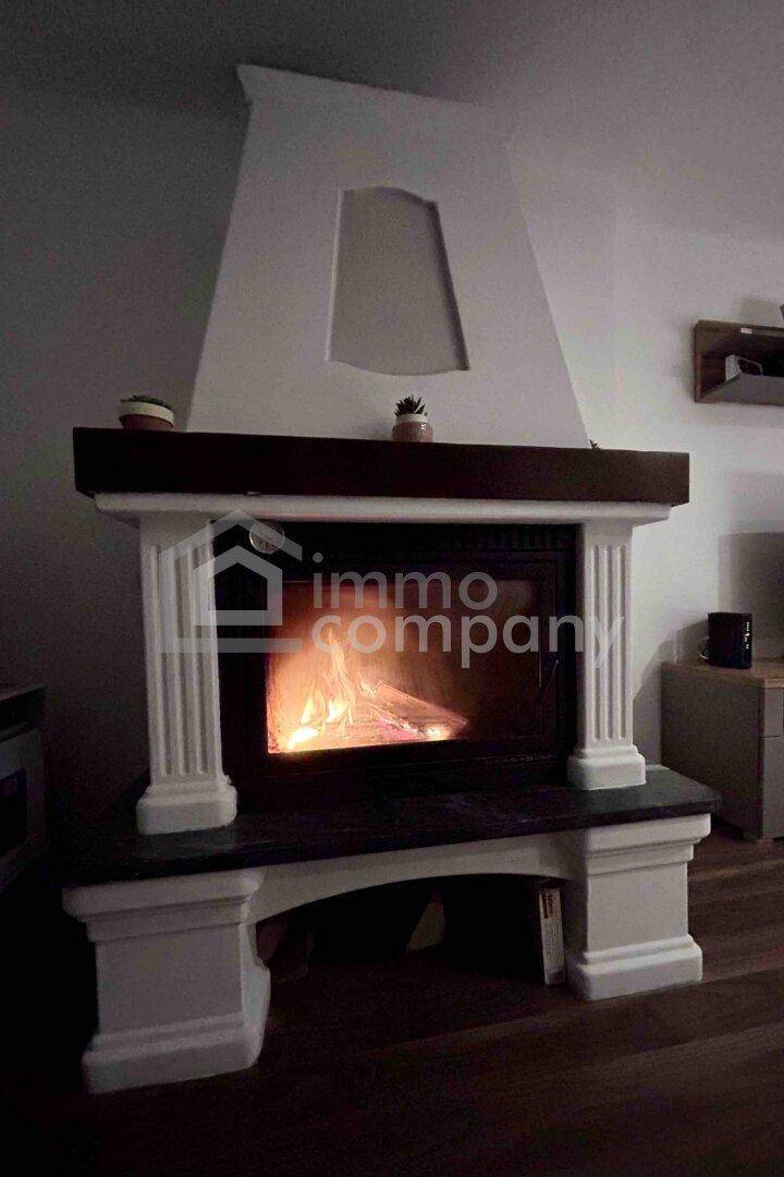 Klassischer Kamin mit brennendem Feuer, umgeben von dekorativen Säulen und einer Holzplatte.