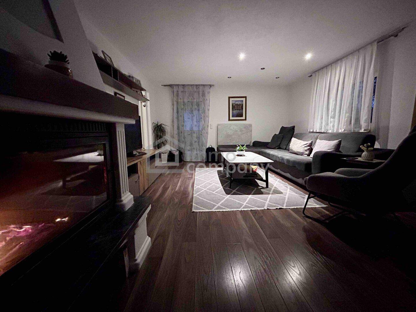 Geräumiges Wohnzimmer mit dunklem Holzboden, Kamin und gemütlicher Sitzecke.