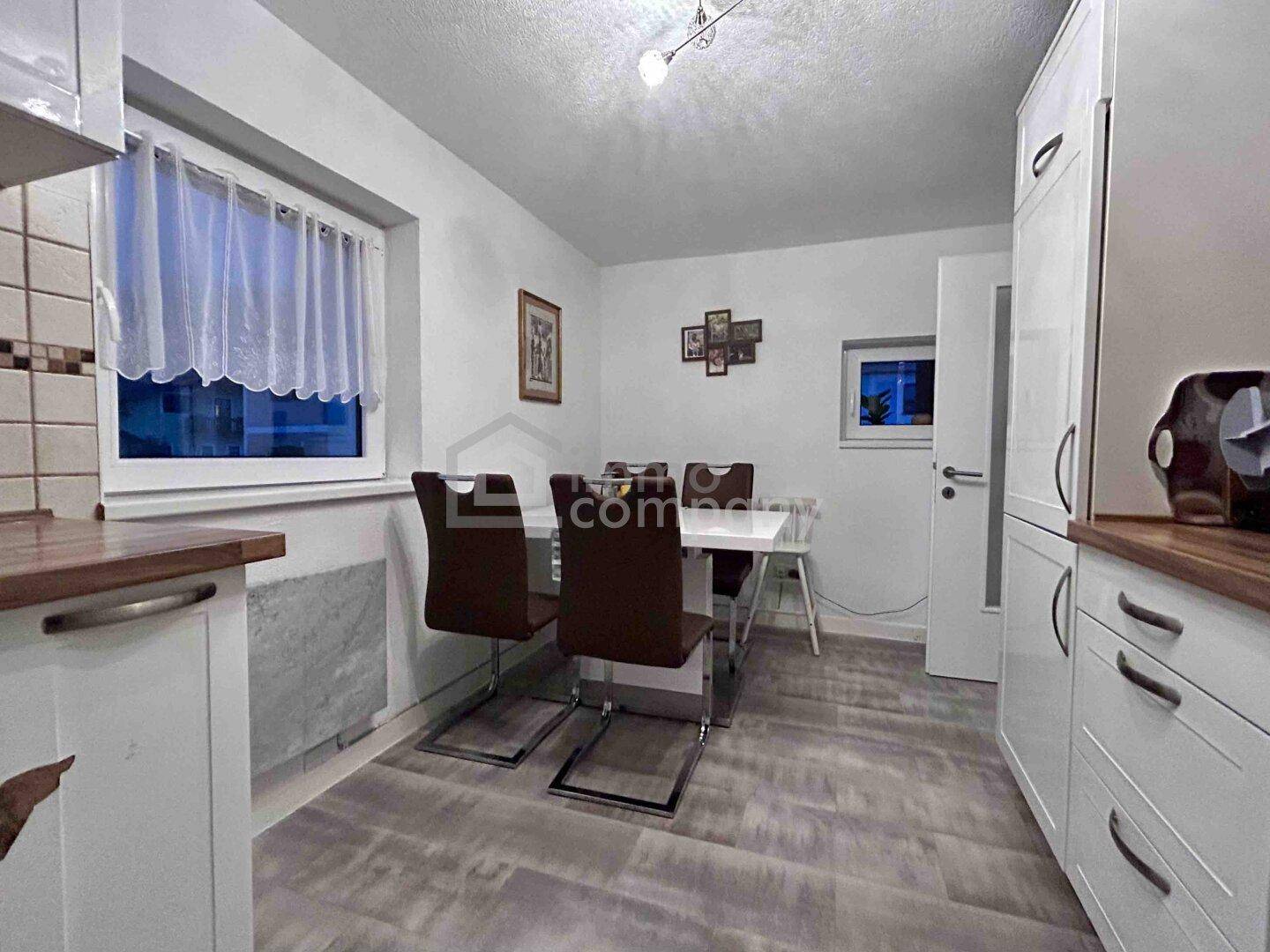 Helle Küche mit weißen Schränken, Holzarbeitsplatten und Essbereich am Fenster.