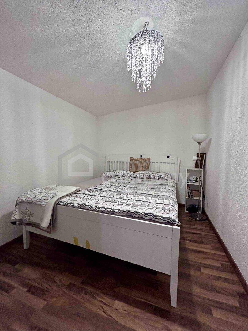 Gemütliches Schlafzimmer mit weißem Holzbett, dunklem Laminatboden und einem modernen Kronleuchter.
