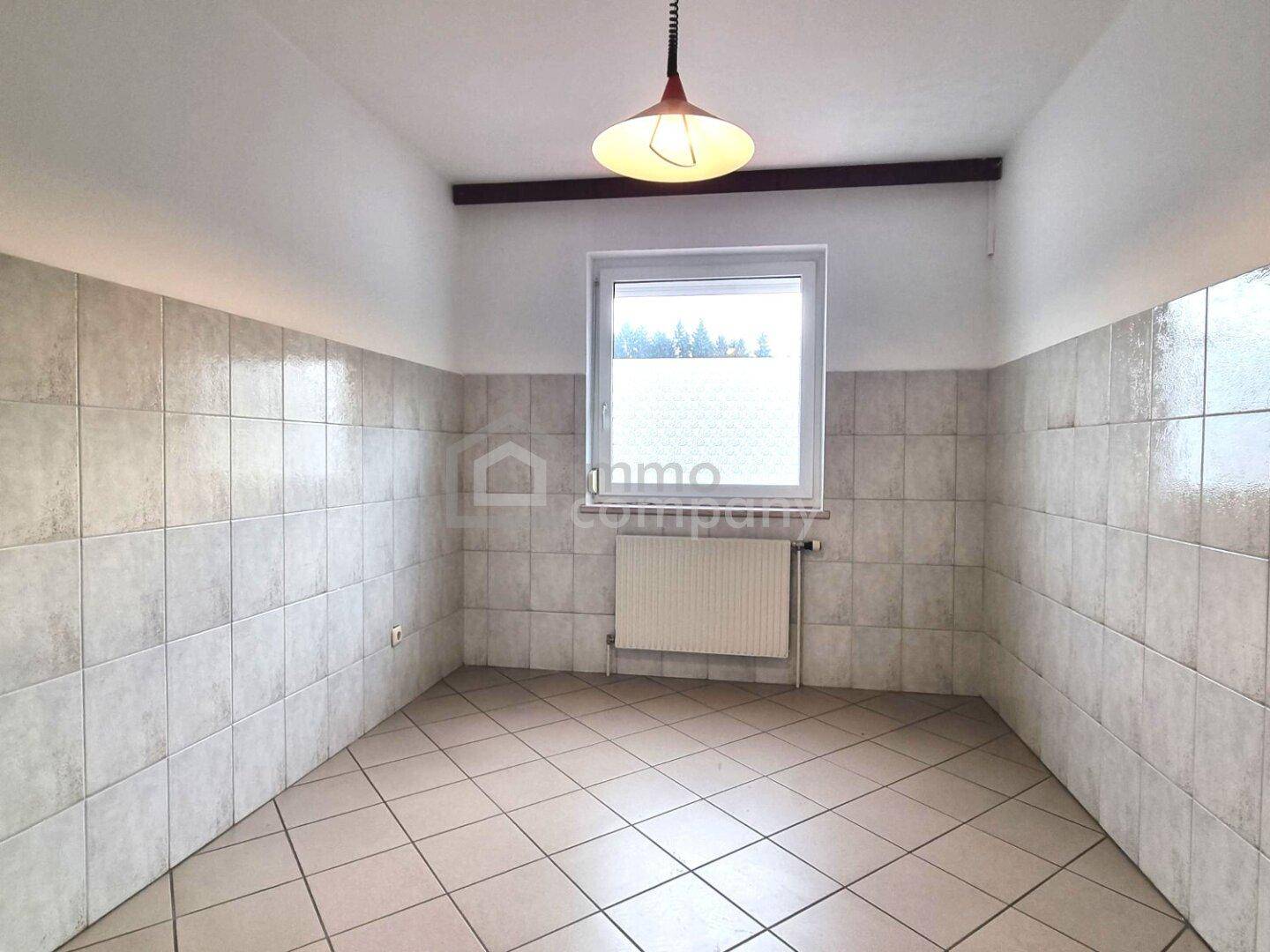 Kleiner, heller Raum mit Fliesenboden und gefliesten Wänden, einem Fenster und Blick ins Grüne.