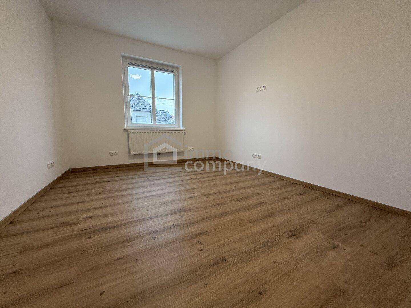Helles, leeres Zimmer mit Laminatboden und Fenster, bereit zur individuellen Gestaltung.