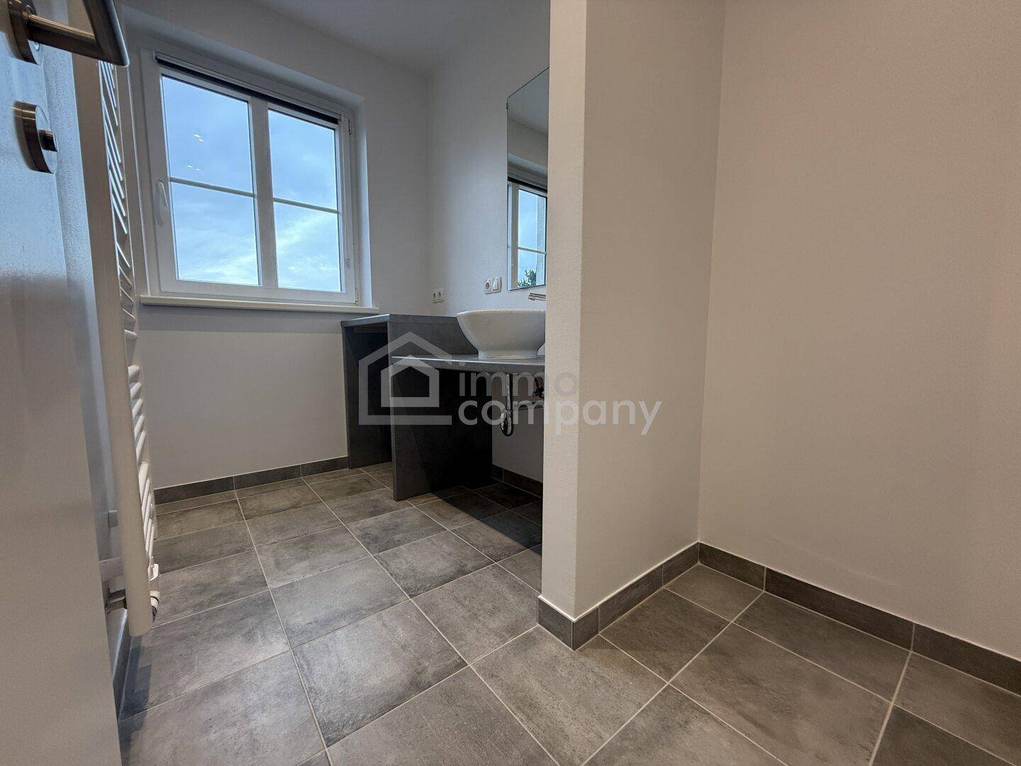 Modernes Badezimmer mit grauen Fliesen, Waschbecken und Fenster für Tageslicht.
