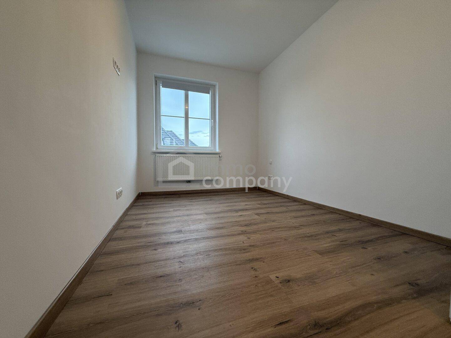 Leeres Zimmer mit Laminatboden und einem Fenster, ideal als Schlaf- oder Arbeitszimmer.