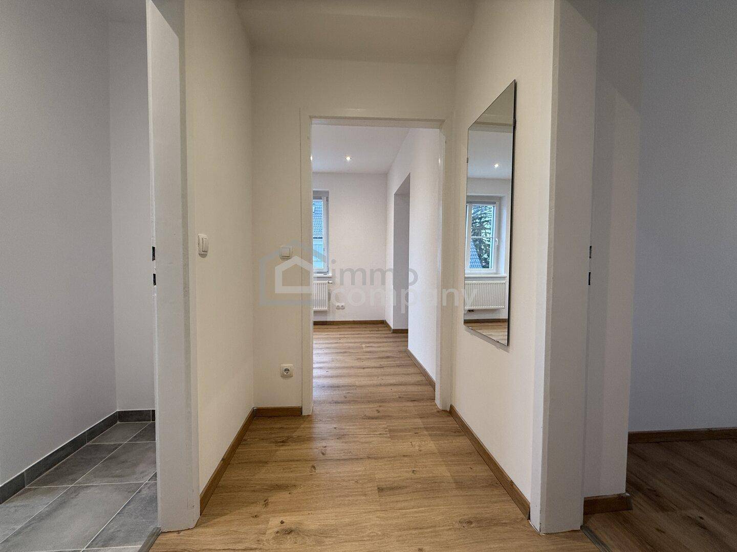 Heller Flur mit Laminatboden und einem Spiegel, der zu weiteren Räumen führt.