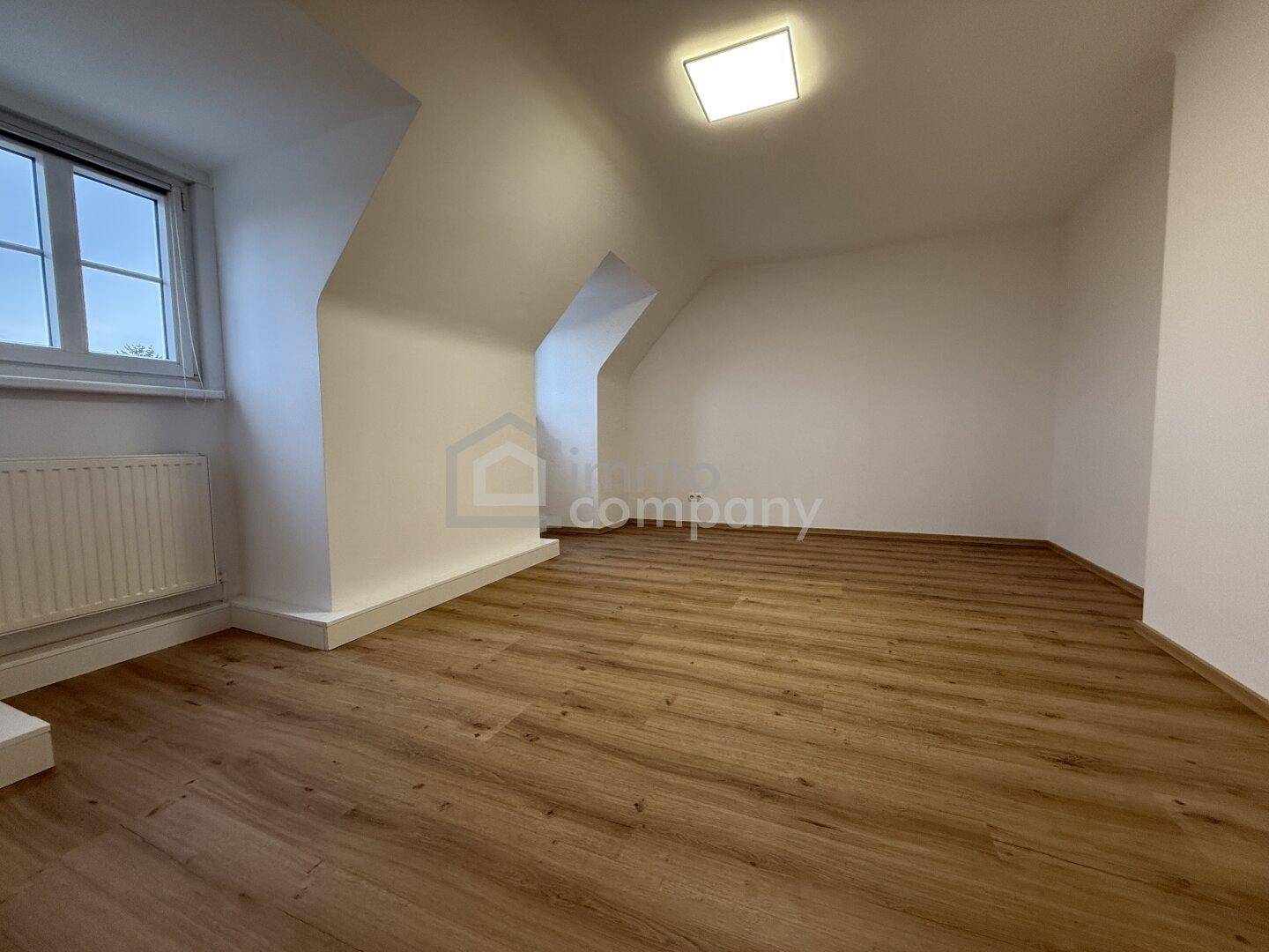 Geräumiges Zimmer im Dachgeschoss mit Laminatboden, Dachschrägen und Fenster.