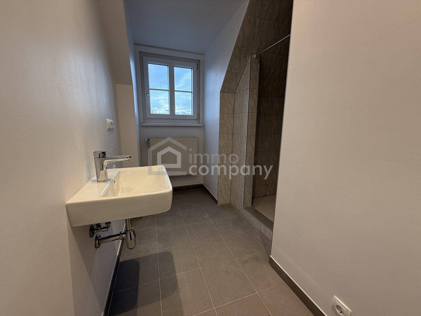 Kompaktes Badezimmer im Dachgeschoss mit Dusche, Waschbecken und Fenster.