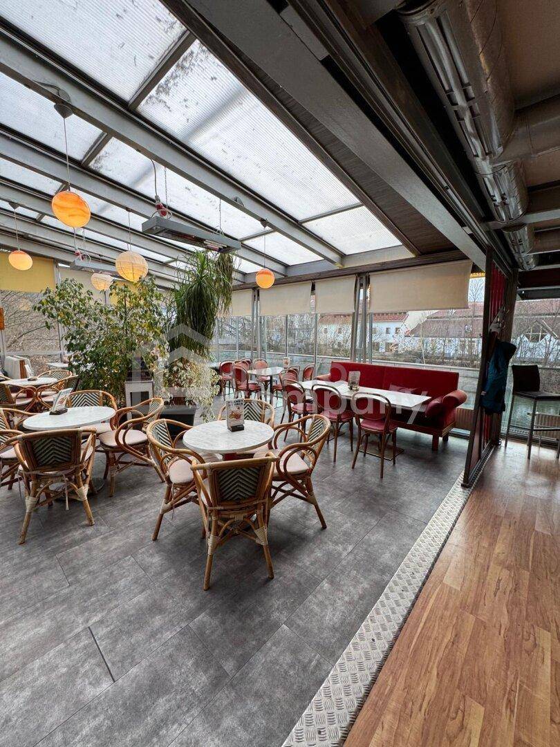 Heller Gastraum mit Glasdach, verschiedenen Sitzbereichen und Holzboden, ideal für Restaurantbetrieb.