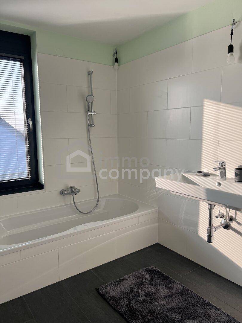 Helles Badezimmer mit Badewanne, Dusche, Waschbecken und Fenster, weiße und hellgrüne Wände.
