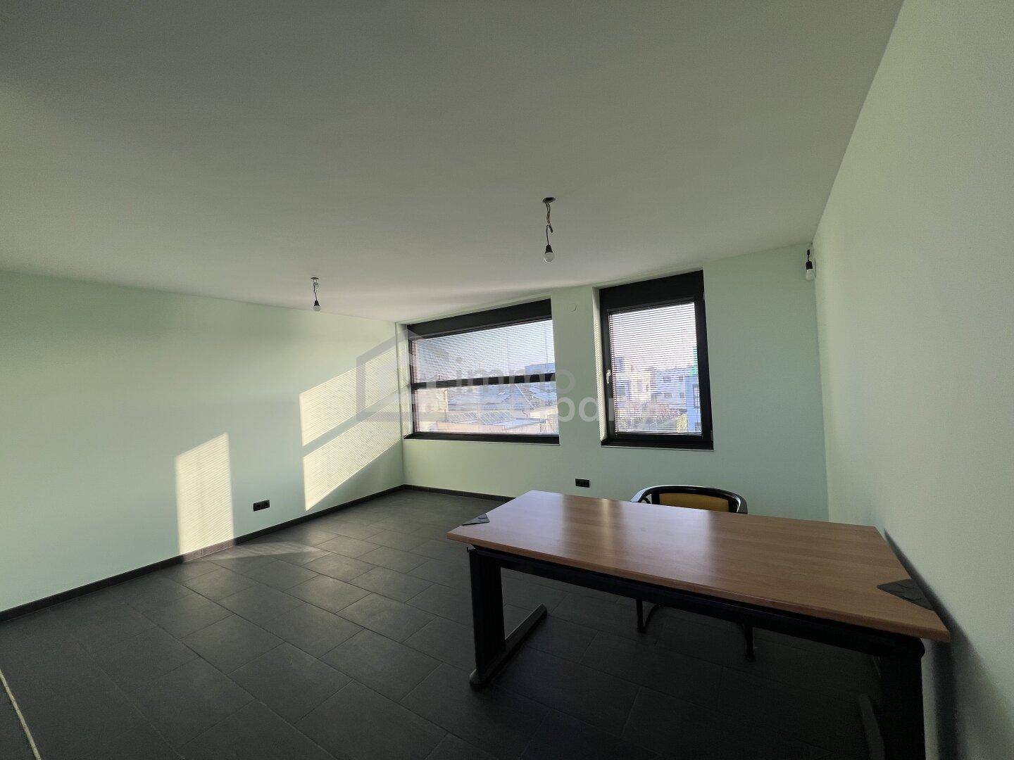 Helles Büro mit dunklen Fliesen, hellgrünen Wänden und einem Schreibtisch am Fenster.