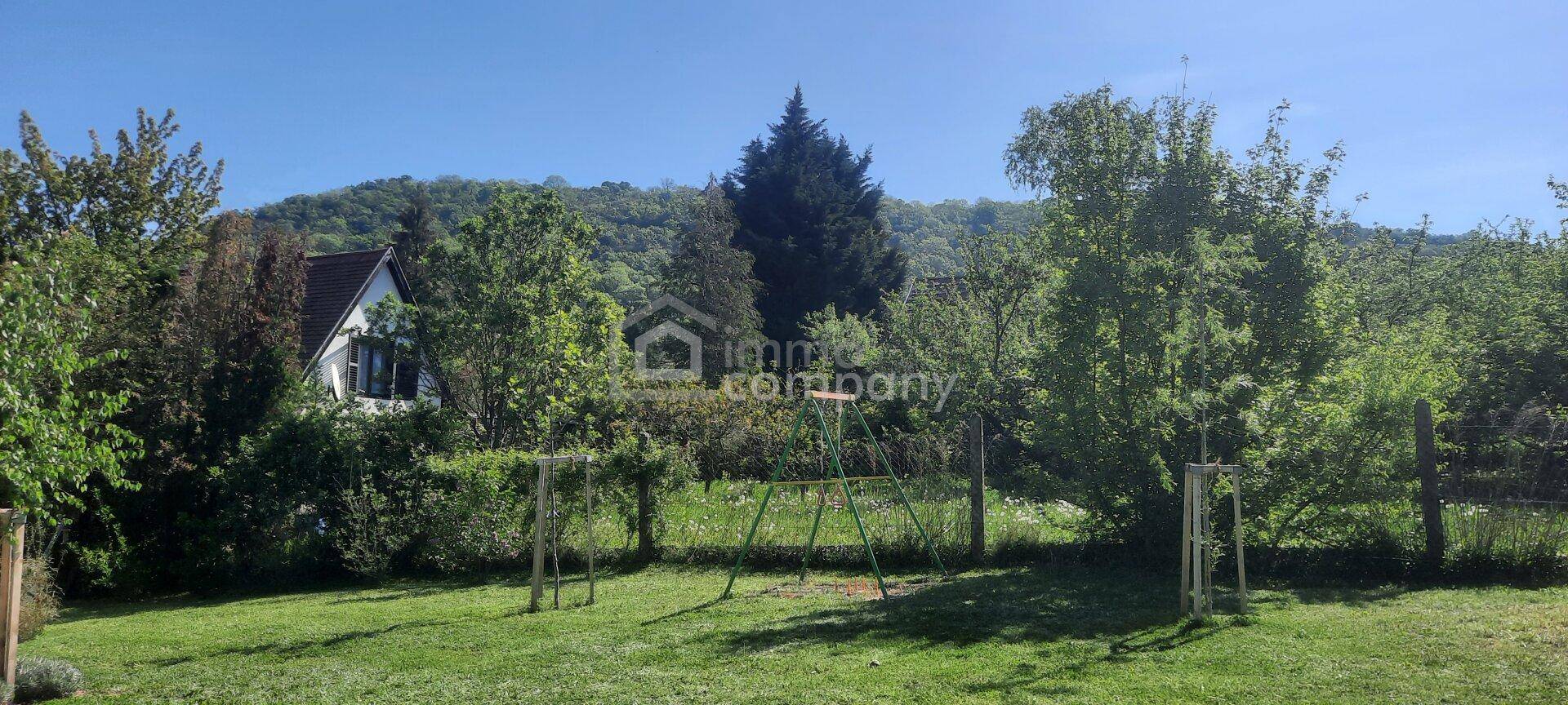 Großer grüner Garten mit Schaukel und Bäumen, umgeben von Natur und Hügeln.