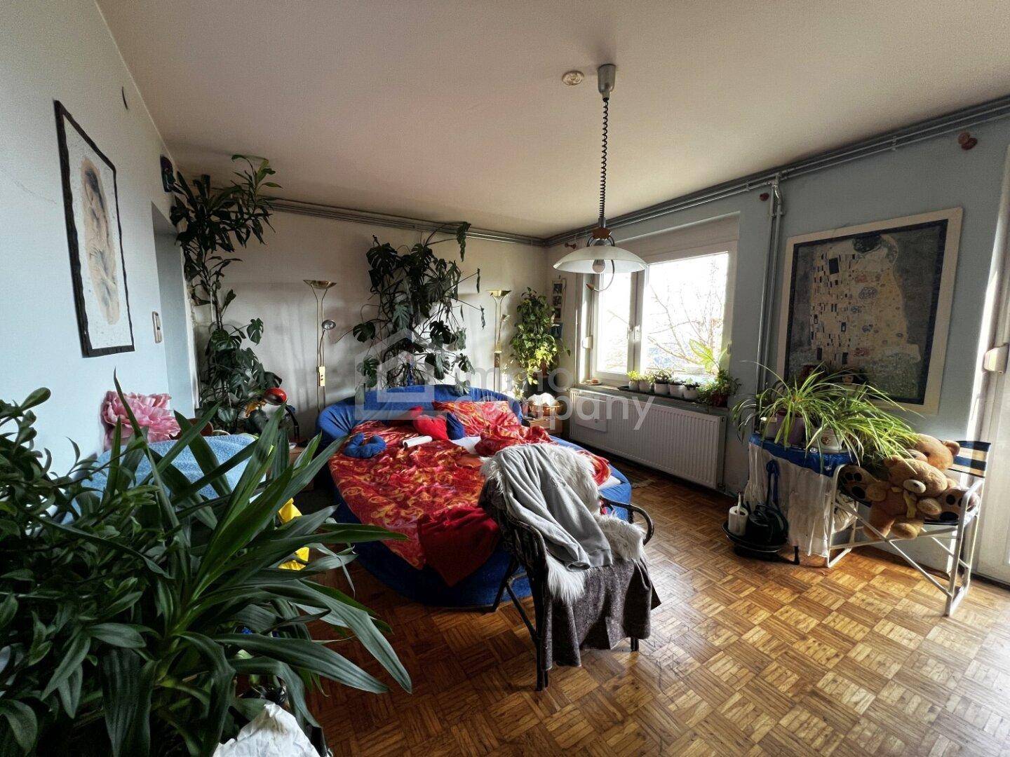 Helles Wohnzimmer mit Parkettboden, vielen Pflanzen und großen Fenstern.