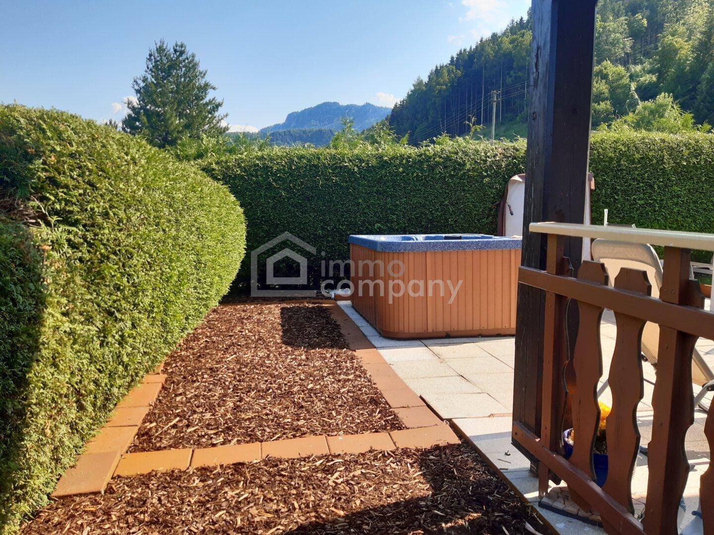 Privater Gartenbereich mit Whirlpool und hoher Hecke, umgeben von grüner Landschaft.