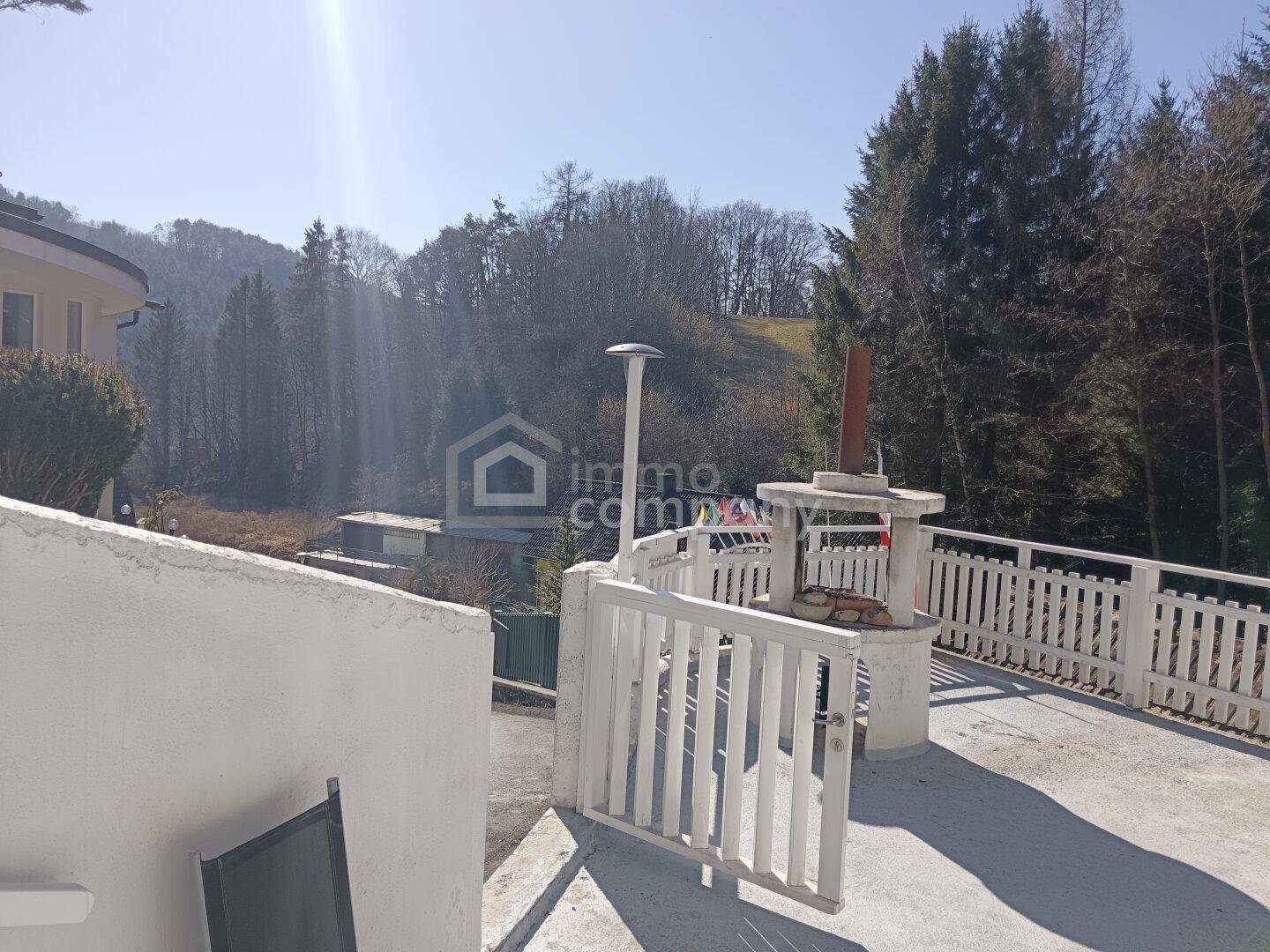 Helle Außenterrasse mit Grillplatz und weitem Blick auf die bewaldete Hügellandschaft.
