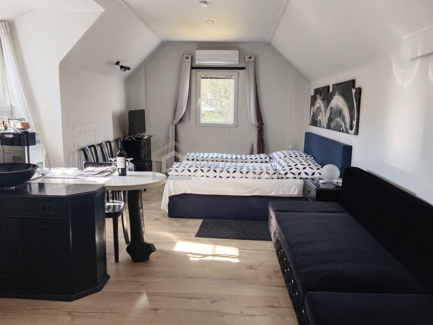 Helles Schlafzimmer im Dachgeschoss mit Doppelbett, Sofa und Klimaanlage.