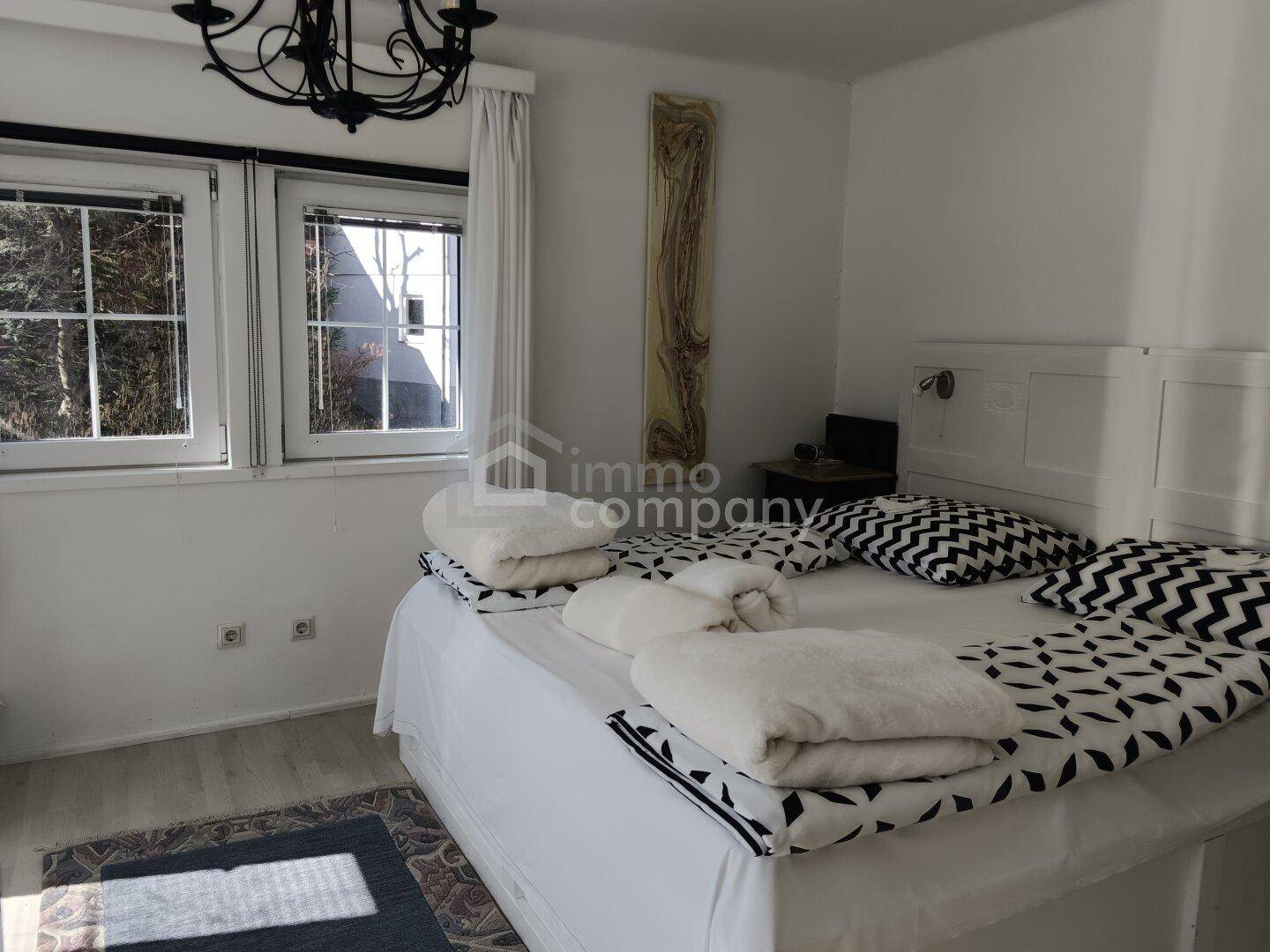 Gemütliches Schlafzimmer mit großem Doppelbett, zwei Fenstern und Teppich.