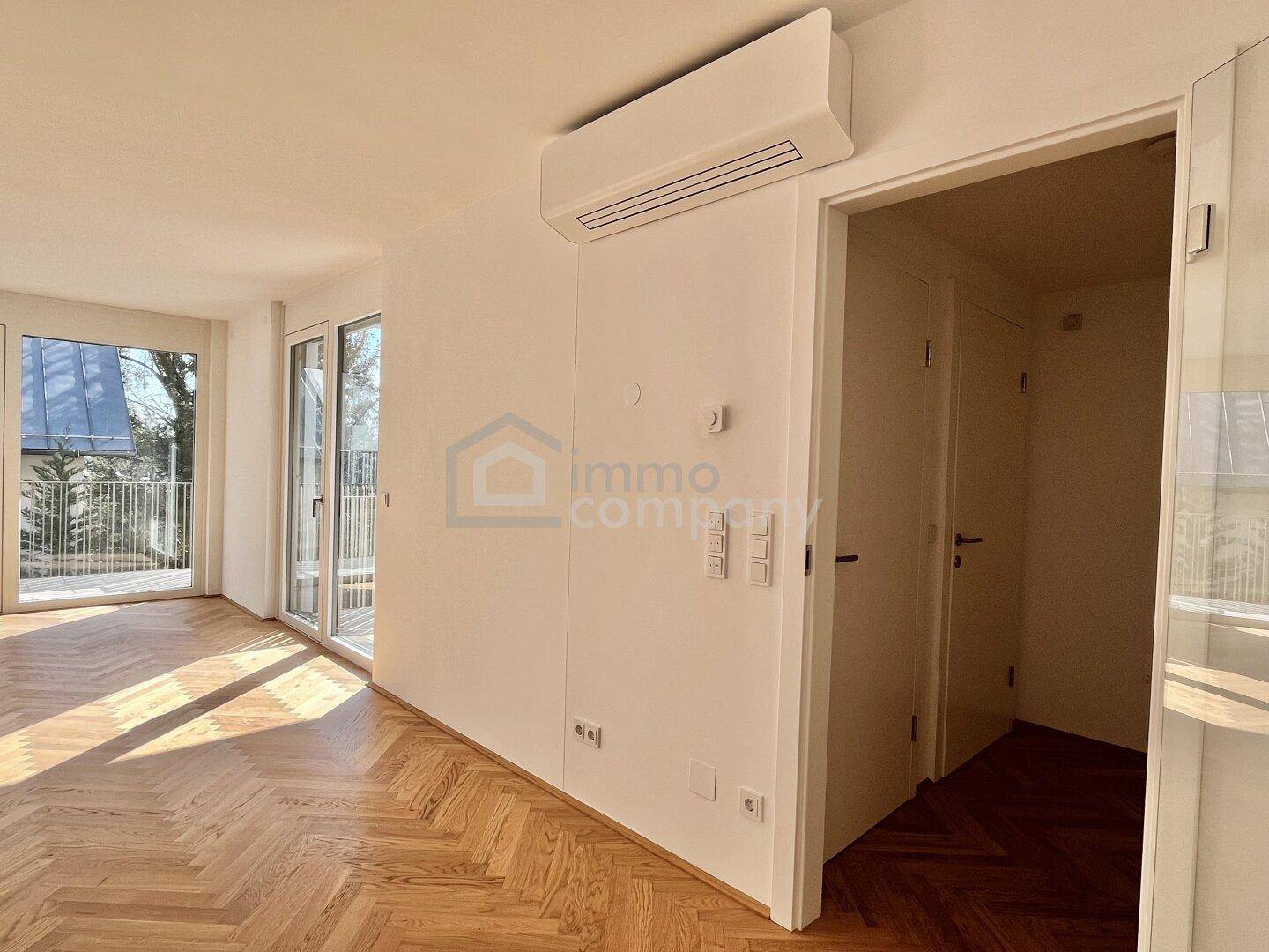 Heller Raum mit Fischgrätparkett, Klimaanlage und Zugang zu einem Balkon.