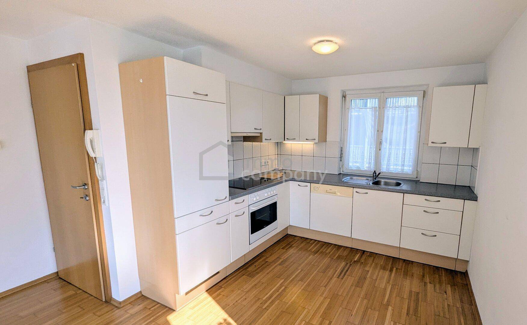 Funktionale Küche mit weißen Einbauschränken, Herd und Spüle, ausgestattet mit einem Fenster für natürliches Licht.