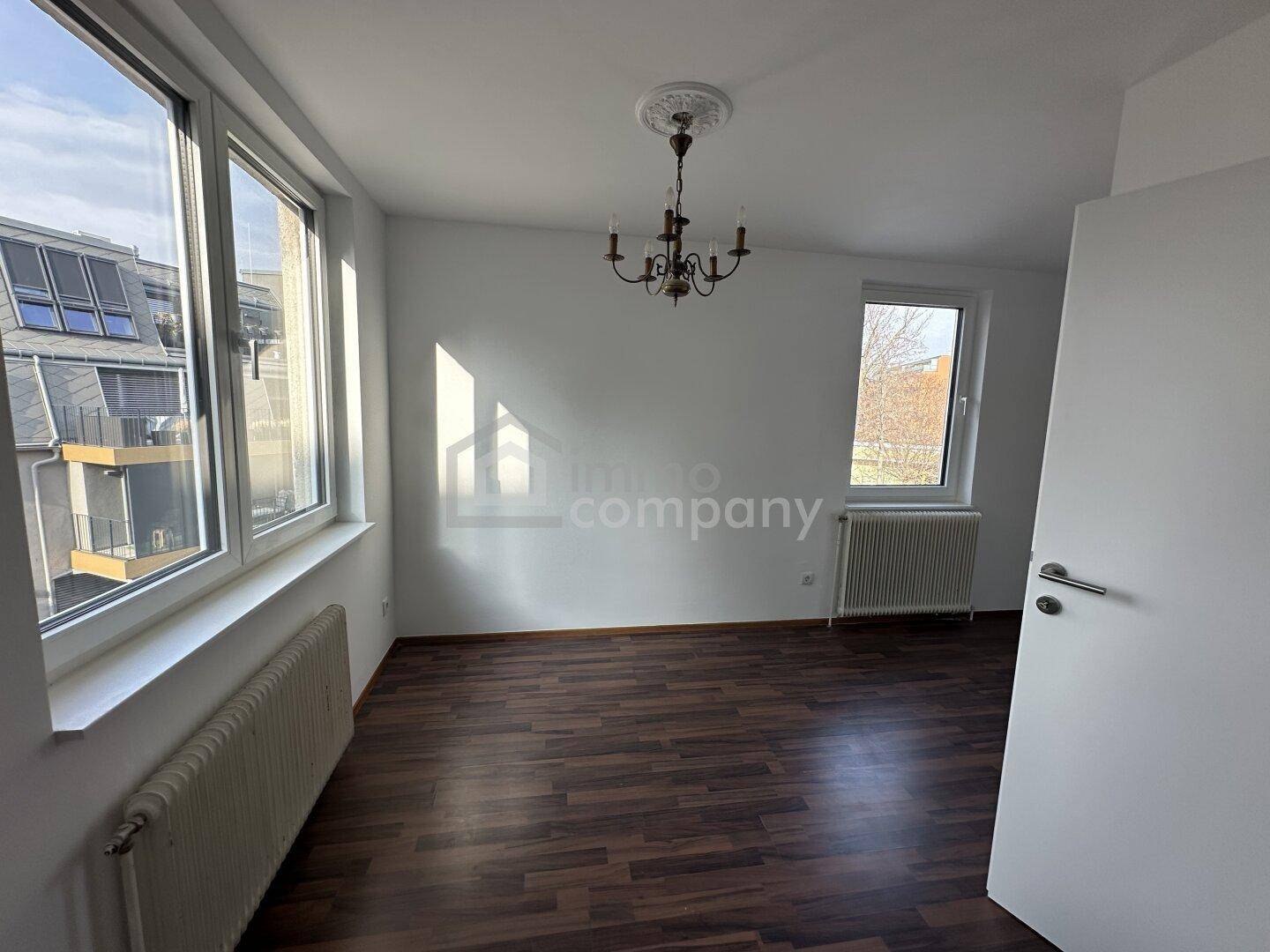 Helles Schlafzimmer mit dunklem Laminatboden, großen Fenstern und Kronleuchter.