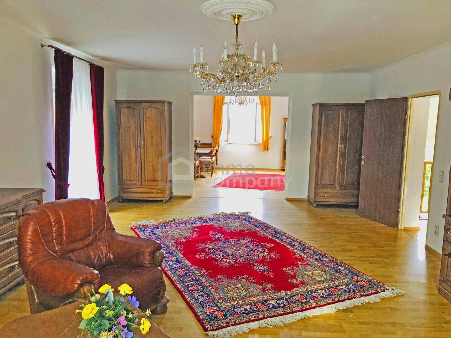 Geräumiges Wohnzimmer mit Parkettboden, klassischem Teppich und elegantem Kronleuchter an der Decke.