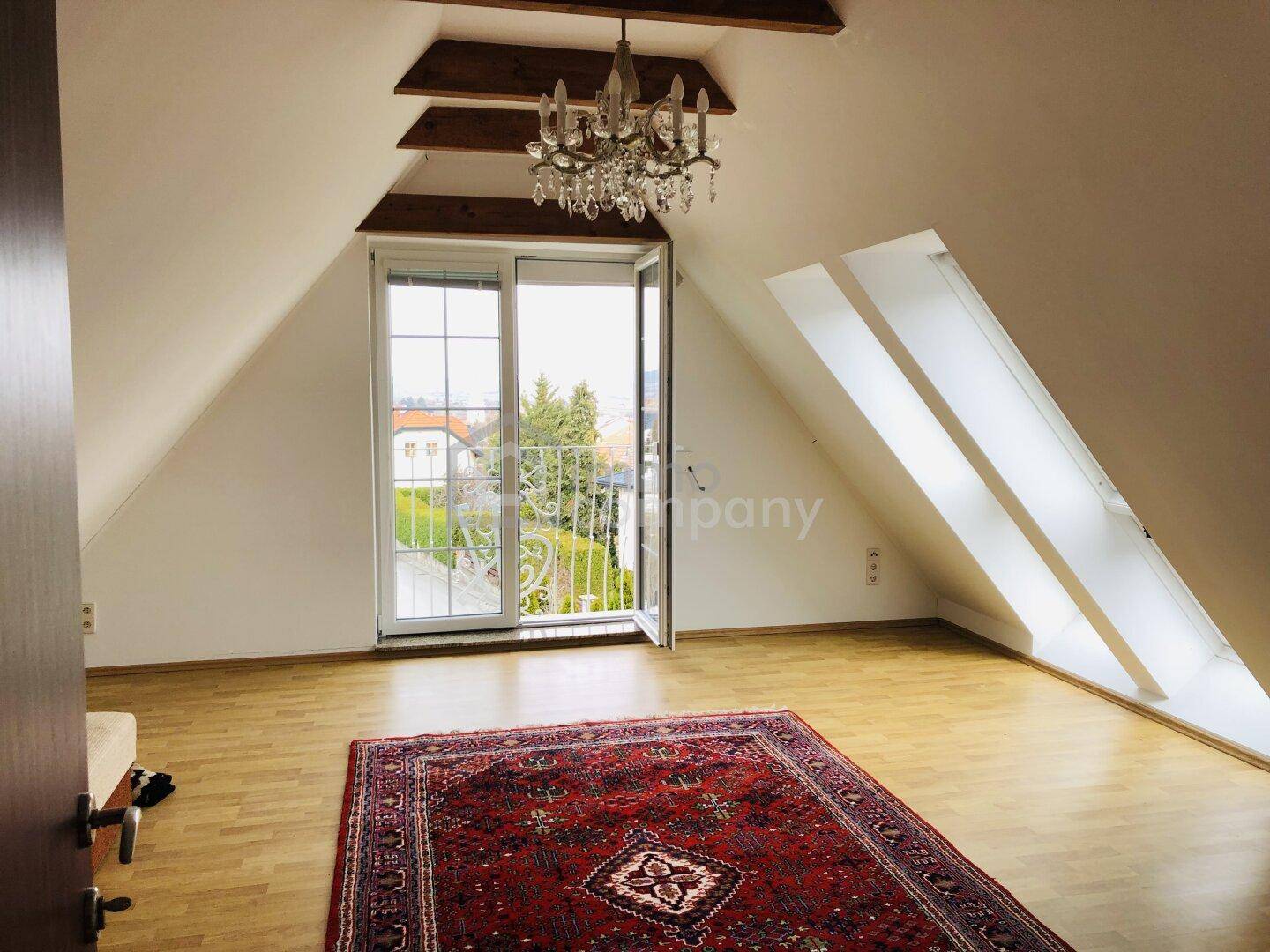 Helles Schlafzimmer im Dachgeschoss mit Holzbalken, Dachfenstern und Zugang zu einem französischen Balkon.