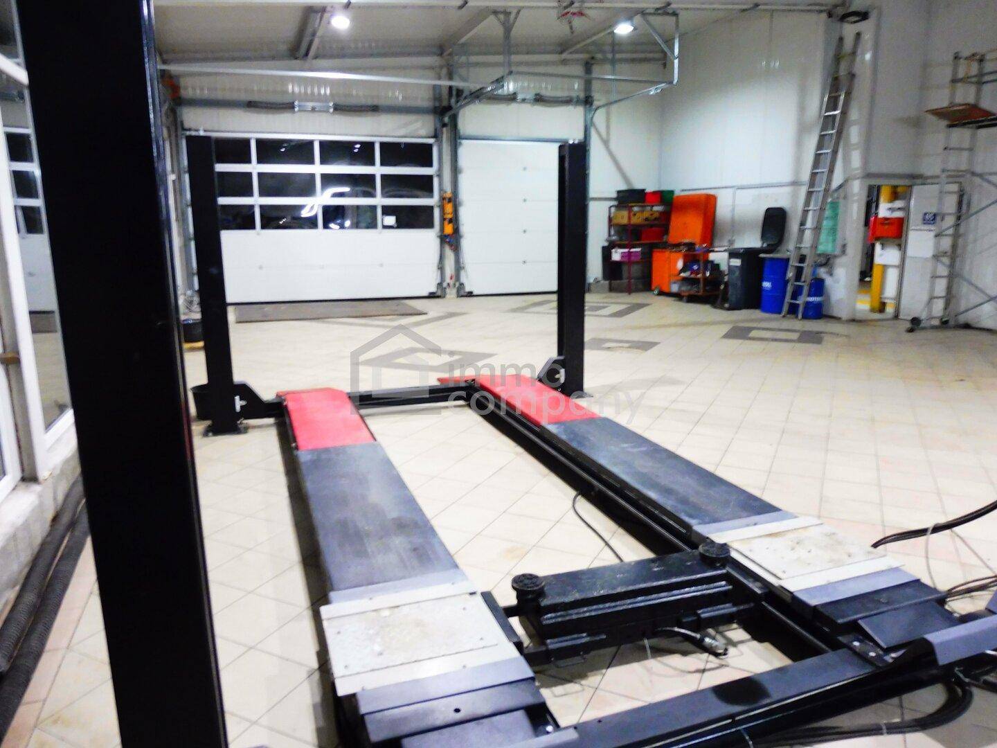Detailansicht einer Hebebühne in der Werkstatt, mit einem Rolltor im Hintergrund und Fliesenboden.