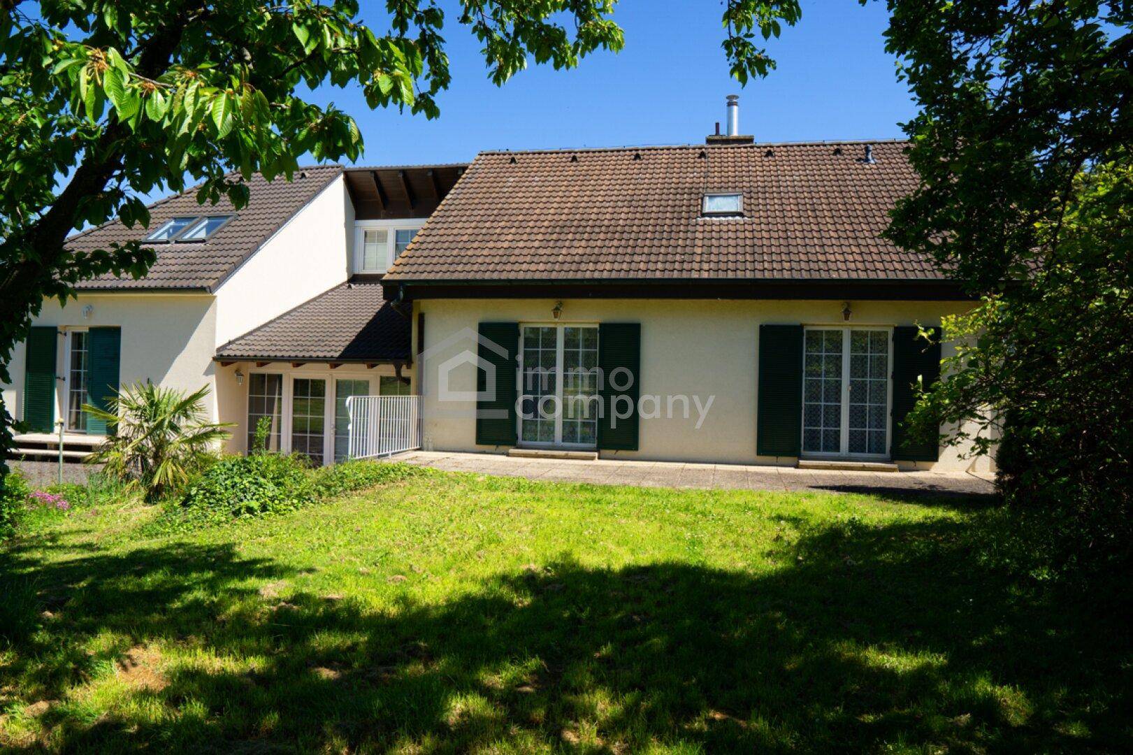 Sonnige Rasenfläche mit Schatten spendenden Bäumen und Blick auf die Rückseite des Hauses.