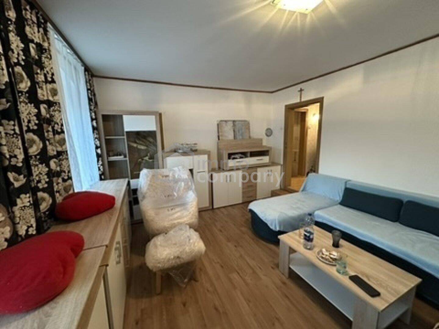 Helles Wohnzimmer mit Sofa, Holzmöbeln und floralen Vorhängen, einladend und komfortabel gestaltet.